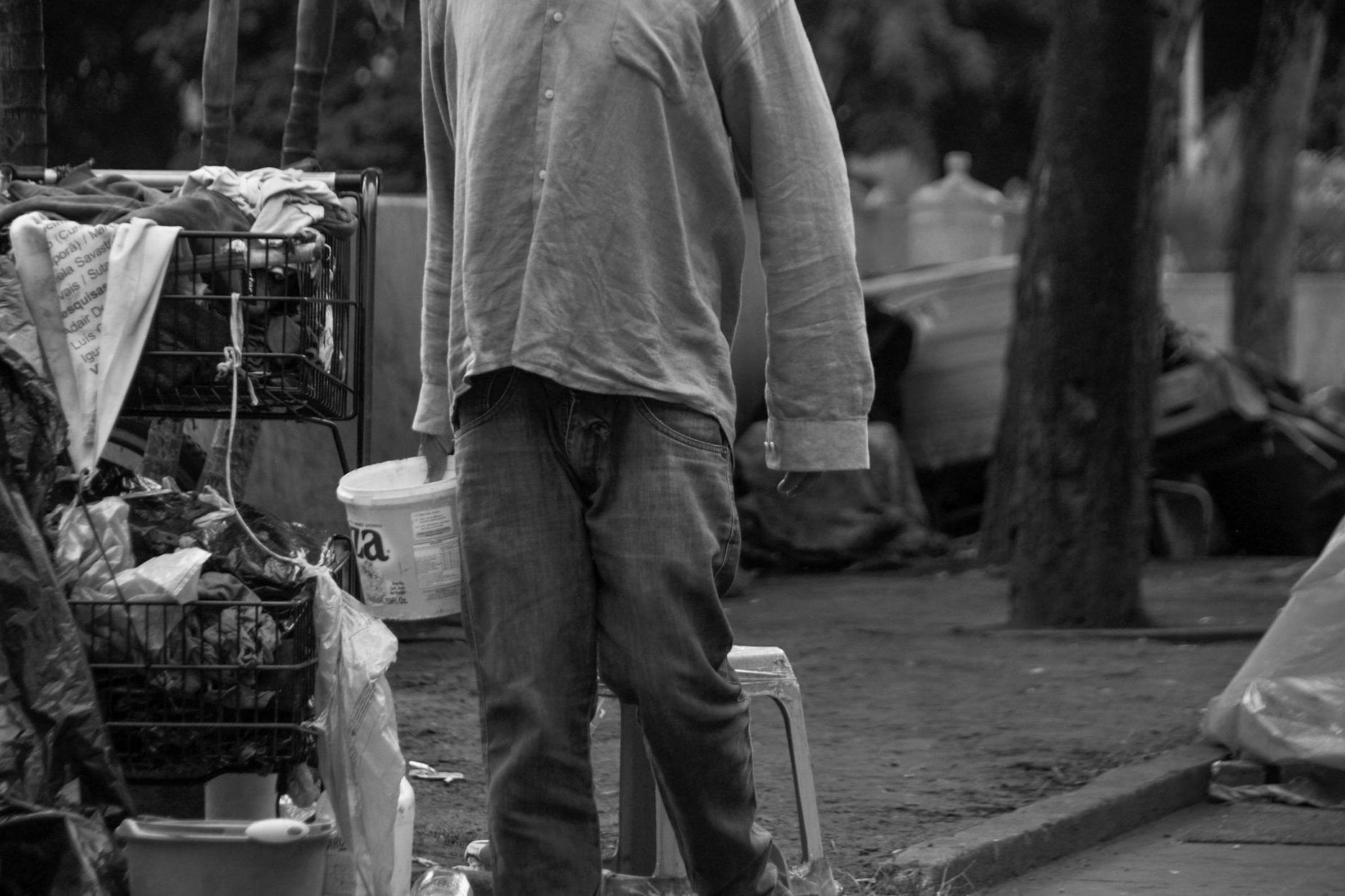 grayscale photo of a person holding a pail beside a trolley full of trash - Streetworking